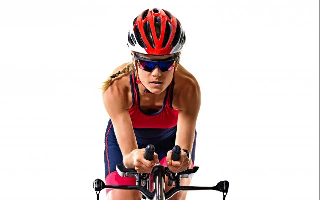 Een wielrenner zit voorover gebogen op haar fiets.