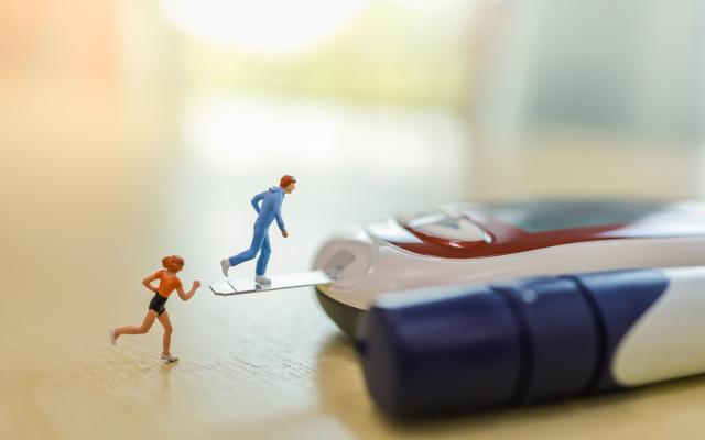 Een glucosemeter en insulinespuit liggen naast elkaar. Twee miniatuurfiguurtjes van hardlopers staan erbij.
