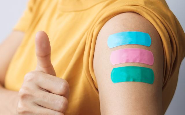 Een persoon met een mondkapje op en drie pleisters op de arm.