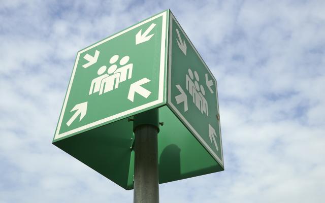 Een vierkant groen bord waarop vier personen zijn afgebeeld. Vanuit de vier hoeken wijzen pijlen naar de groep mensen.