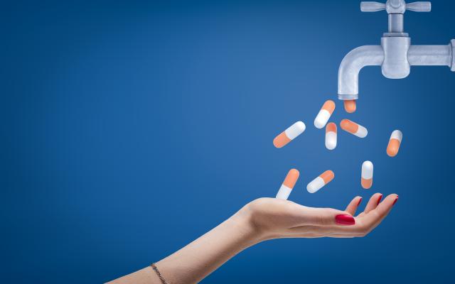 Een hand onder een kraan. Uit de kraan komen pillen.