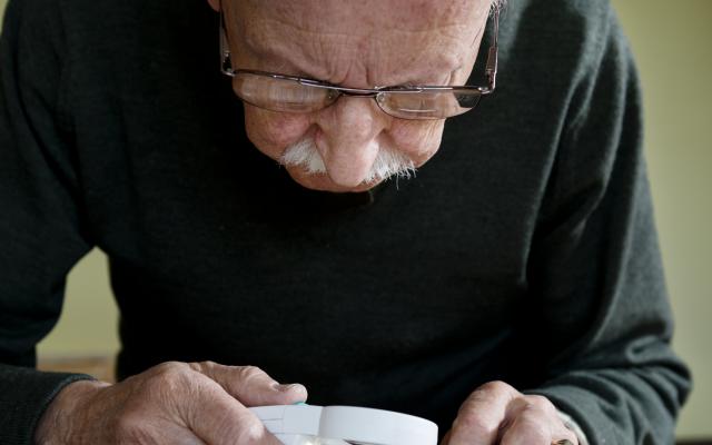 Een oude man staat voorover gebogen. Hij bestudeert iets met een vergrootglas.