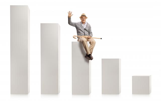 Vijf witte kolommen op een rij, van groot naar klein. Een oudere man met een stok zit op de middelste kolom en zwaait.