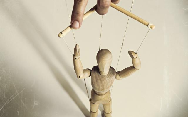 Een hand houdt een houten marionet vast.