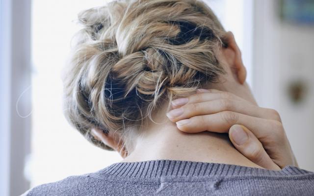 Een vrouw zit voorover gebogen met haar hand in haar nek.