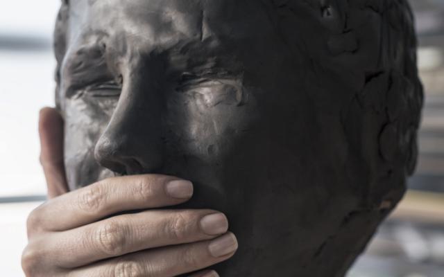 Beeld van een hoofd. Iemand heeft een hand over de mond van het beeld gelegd.