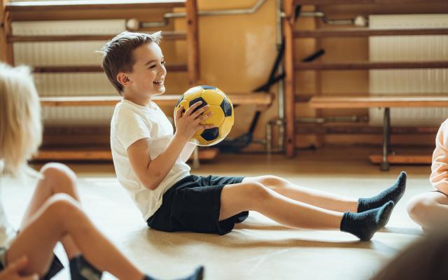 Kinderen zitten op de grond met een voetbal in een gymzaal.