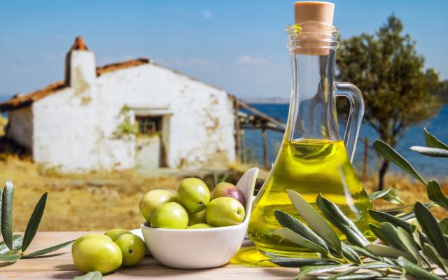 Een fles olijfolie staat naast een schaaltje olijven.