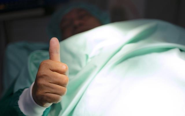 Liggende patiënt die zijn duim omhoog houdt