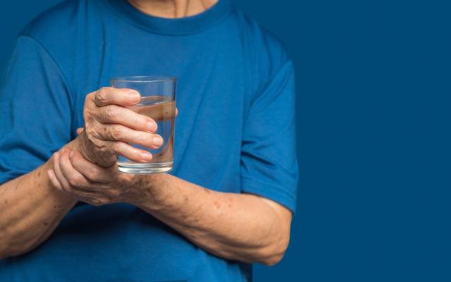 Iemand die een glas water vasthoudt en zijn hand probeert stil te houden