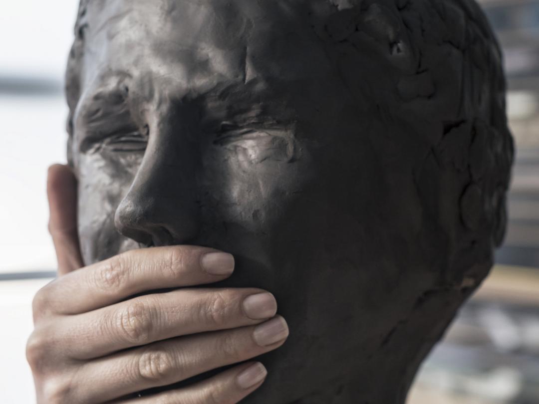 Beeld van een hoofd. Iemand heeft een hand over de mond van het beeld gelegd.