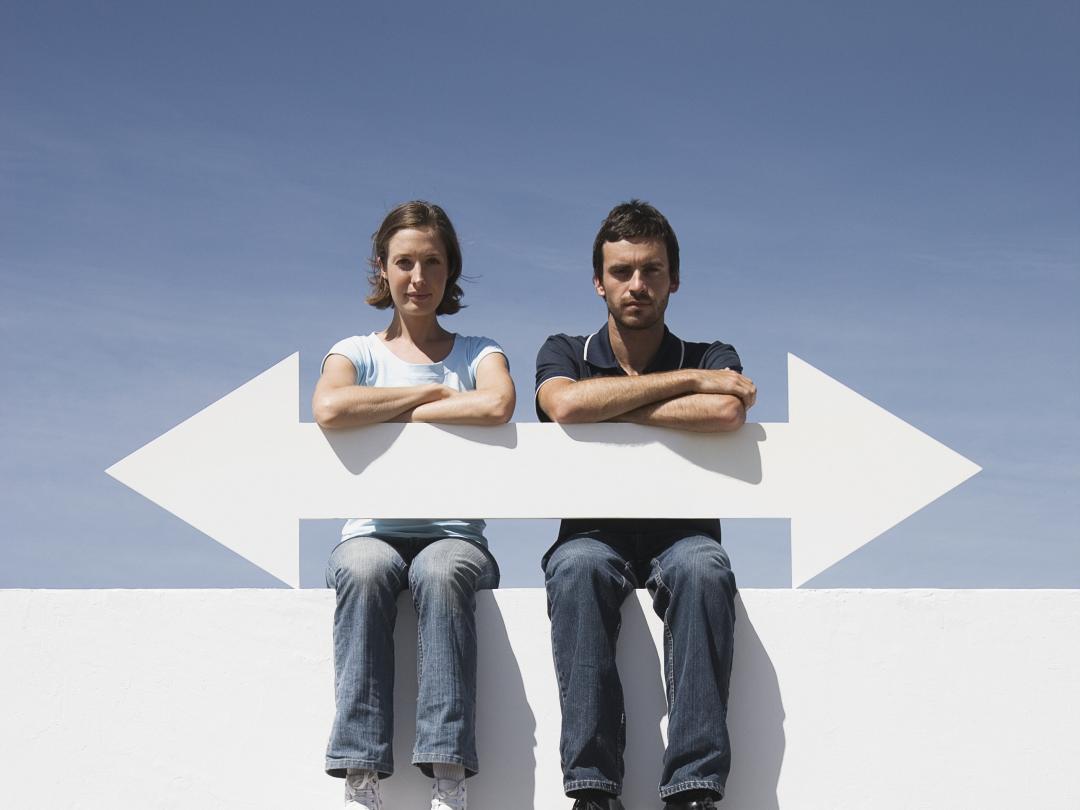 Twee mensen zitten op een muur en houden een pijl vast. De pijl wijst zowel naar links als naar rechts.