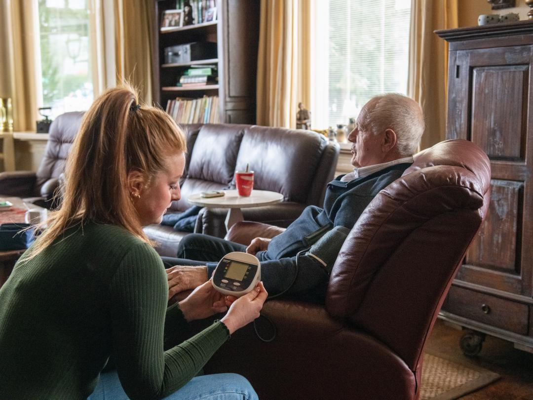 Een verzorger die bloeddruk meet bij oudere