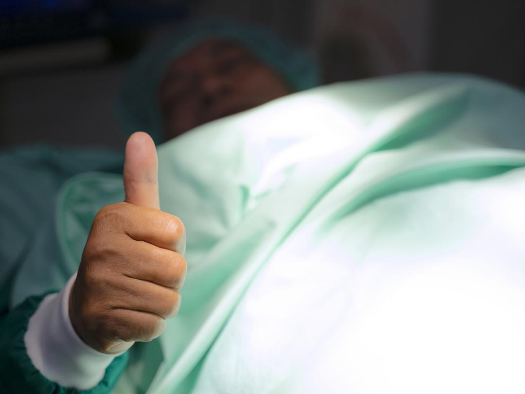 Liggende patiënt die zijn duim omhoog houdt