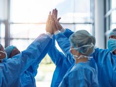 Een groepje artsen, gehuld in beschermende kleding, geeft elkaar een high five.