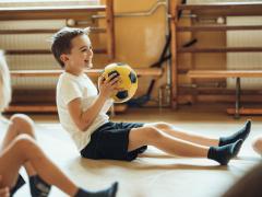 Kinderen zitten op de grond met een voetbal in een gymzaal.