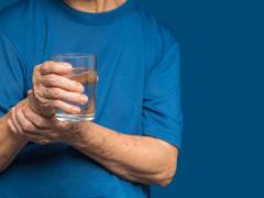 Iemand die een glas water vasthoudt en zijn hand probeert stil te houden